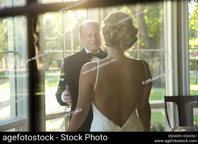 Bride and father of the bride about to embrace celebrating the wedding day, seen through window