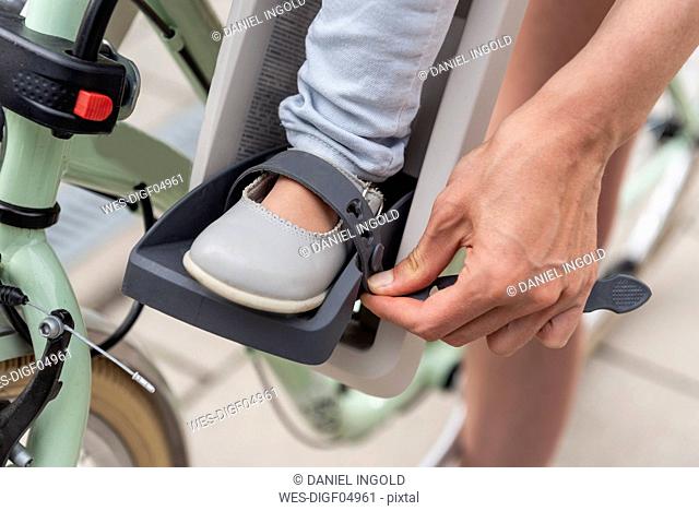 Child sitting in children's seat, mother fastening safety belt