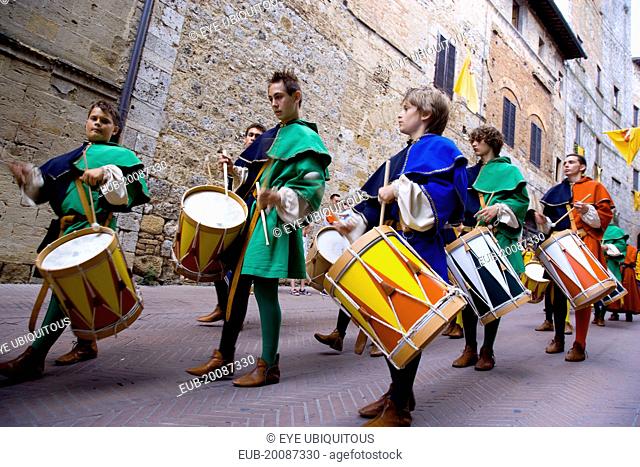 Boys and young men in Medieval costume beating drums in a parade through the streets during a pageant in the town