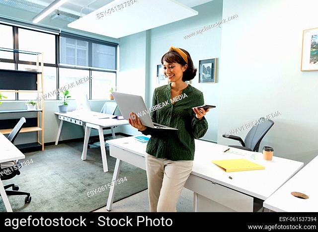 Asian female architect with smart phone using laptop in creative office