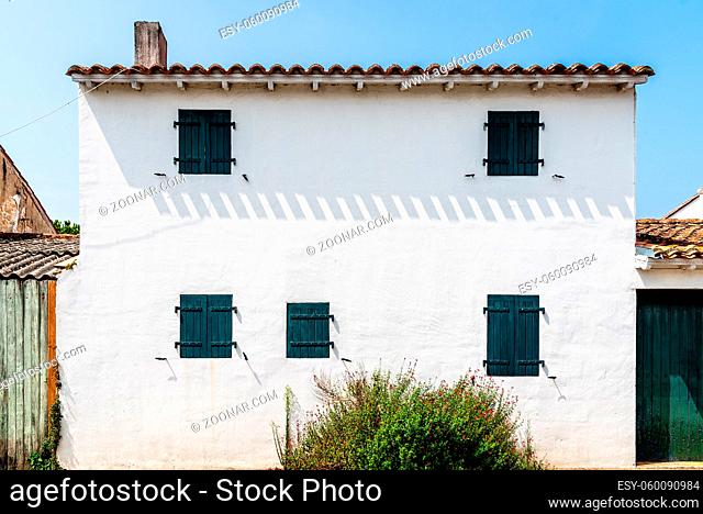 White facade with green windows with closed shutters of traditional house in the Island of Re decorated with colorful flowers