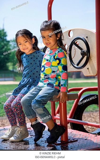 Portrait of two girls sitting on playground climbing frame