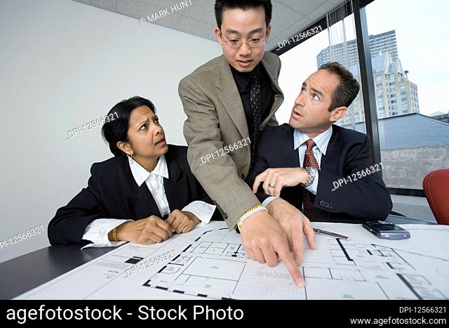 Three business executives discussing a blueprint