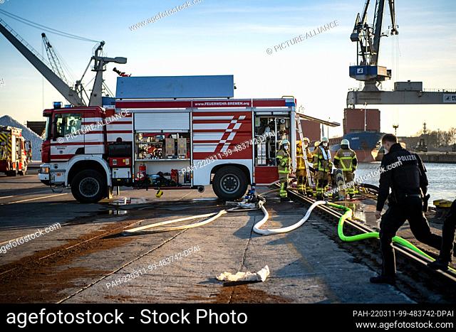 11 March 2022, Bremen: Emergency forces of the fire department and the police stand at the port. A large pile of peat caught fire in the industrial ports
