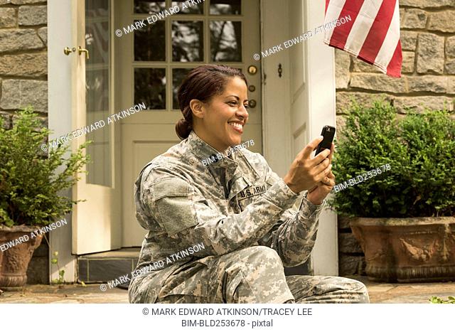 Smiling African American soldier sitting on front stoop texting on cell phone