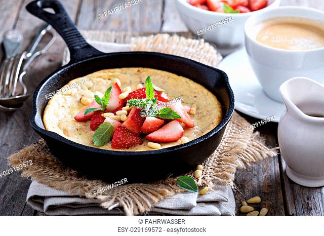 Baked pancake in cast iron pan with fresh strawberries and pine nuts