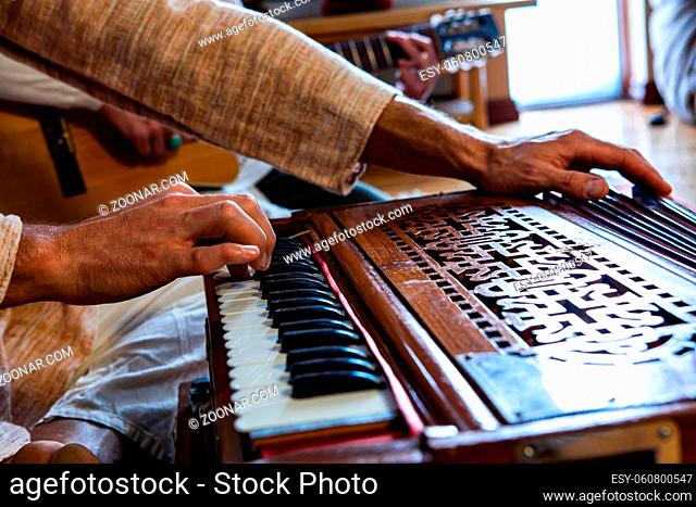 Closeup of male shamanic hands playing sacred kirtan music with fingers on keys of harmonium while sitting in room for peaceful meditation