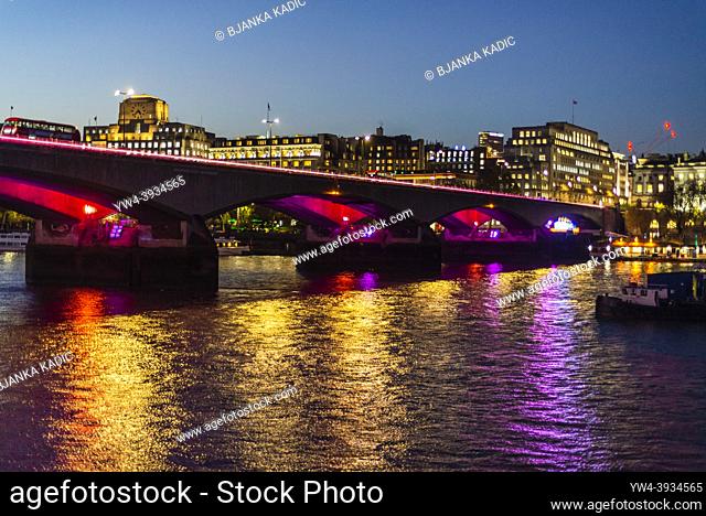 London Bridge lit at night casting colours light on the river Thames, London, England, UK