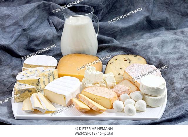 Varieties of cheeses on chopping board with carafe of milk on textile