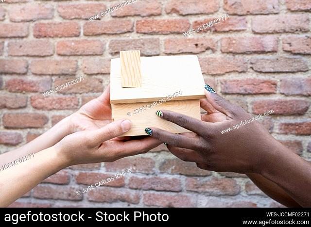 Female friends holding house model by brick wall