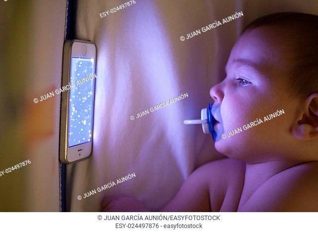 12 month old baby watching a lullaby cartoons with mobile phone on the crib