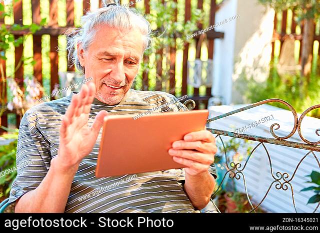 Senior Mann als Rentner mit Tablet Computer online beim Videochat im Garten
