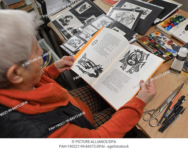 21 February 2019, Brandenburg, Bad Saarow: Gertrud Zucker, a painter, sits in her studio and leafs through her illustrated book ""The Magic Flute""
