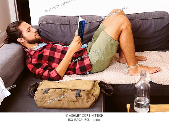 Young man relaxing on sofa, reading book