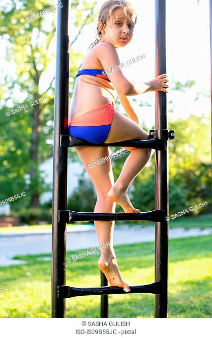 Portrait of girl in bikini sitting on garden climbing frame