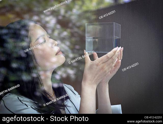Close up female designer looking at cube with liquid at window