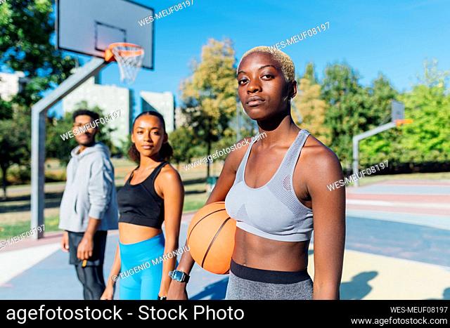 Confident sportswoman with basketball by friends in court