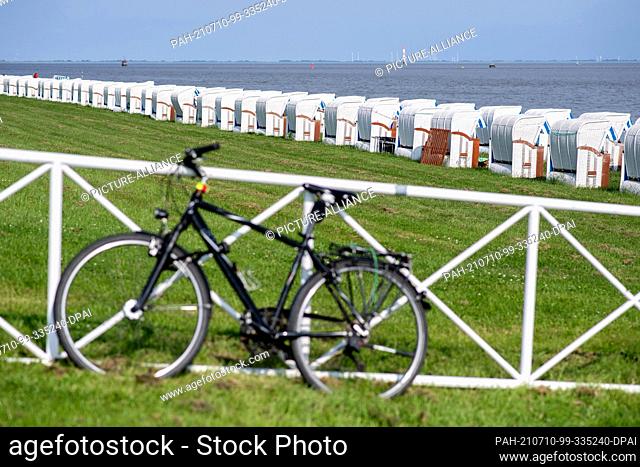 10 July 2021, Lower Saxony, Wilhelmshaven: A man's bicycle leans against a fence on the south beach in sunny weather in front of numerous beach chairs