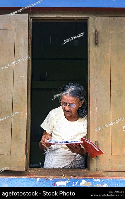 Matara, Sri Lanka An elderly woman reads a Buddhist prayer book in the window of her home