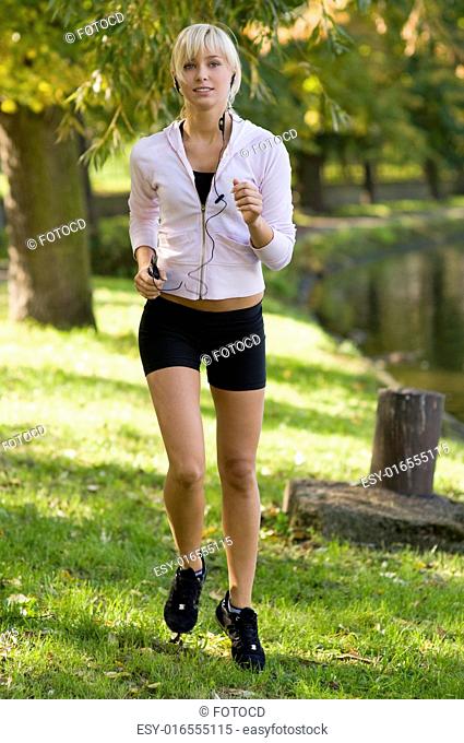 cute young girl running and listening music in park near river almost in sunset
