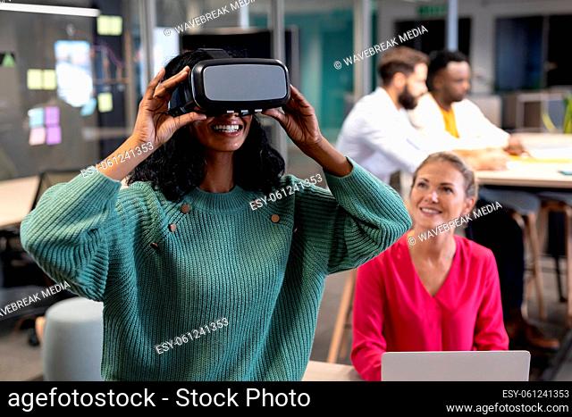 Smiling african american businesswoman wearing vr simulator by caucasian colleague at workplace