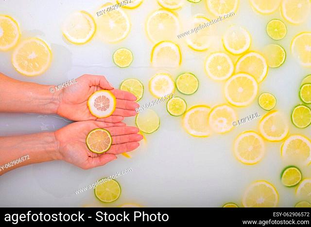 A slice of ripe lime in the hands of a woman. Top view Unrecognizable Girl takes a milk bath with lemons. Citrus spa. Body care. Skin whitening
