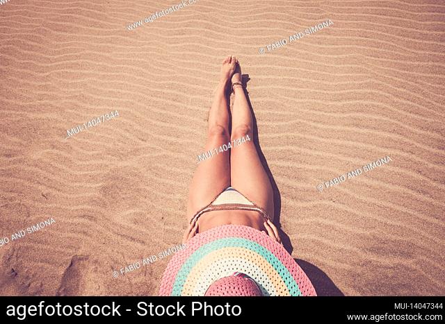 summer time female people have sun bath for tan skin - attractive woman with straw hat lay down on the sand at the beach in bikini swimwear - old style mood...