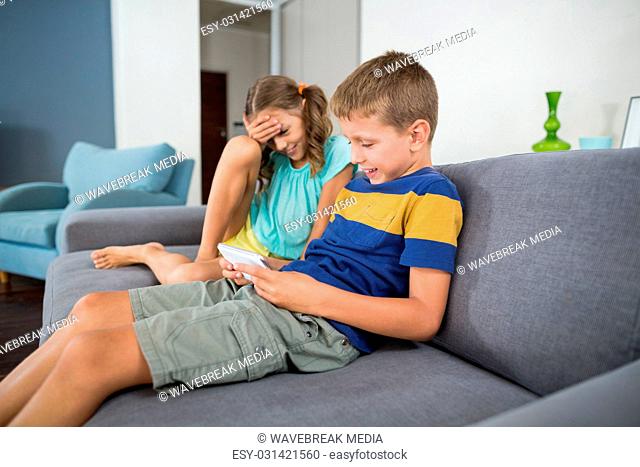 Smiling siblings using digital tablet on sofa in living room