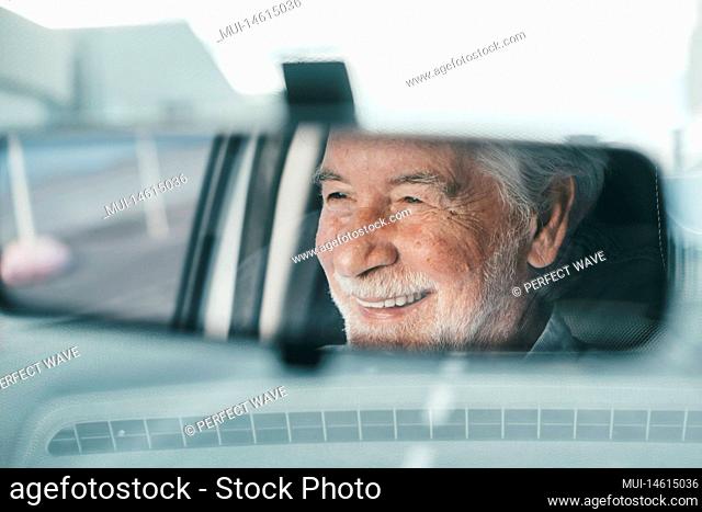 Portrait of one old pensioner man driving and enjoying his new car. Rear view mirror