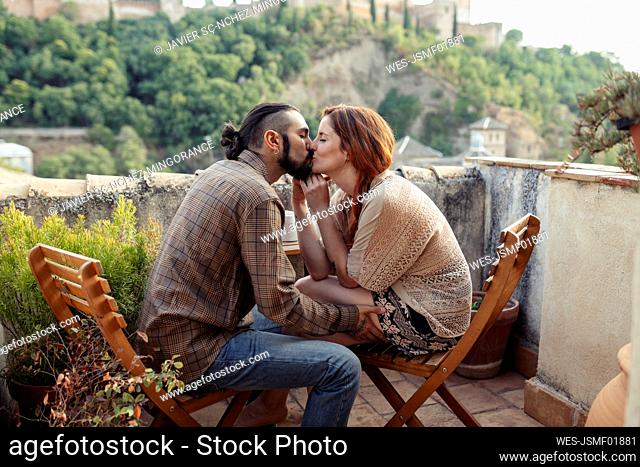 Couple kissing while sitting on chair at rooftop