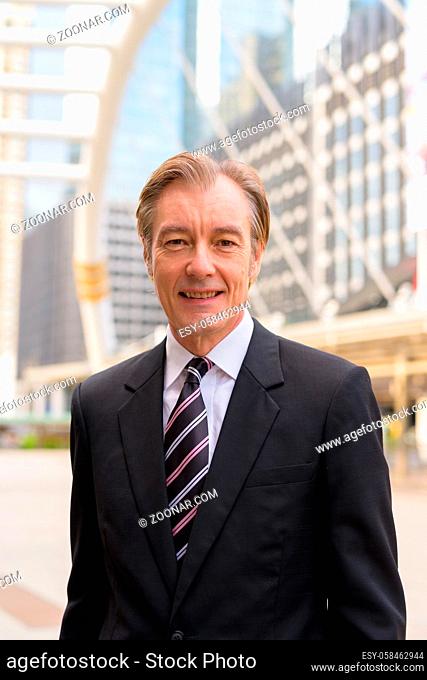 Portrait of mature handsome businessman in suit at skywalk bridge in the city outdoors