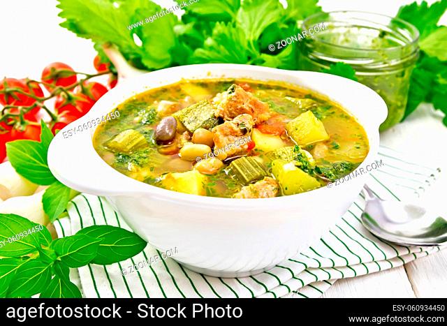 Soup with pisto sauce, lard, tomatoes, zucchini, beans, celery and onions leek in a bowl on a napkin on wooden board background