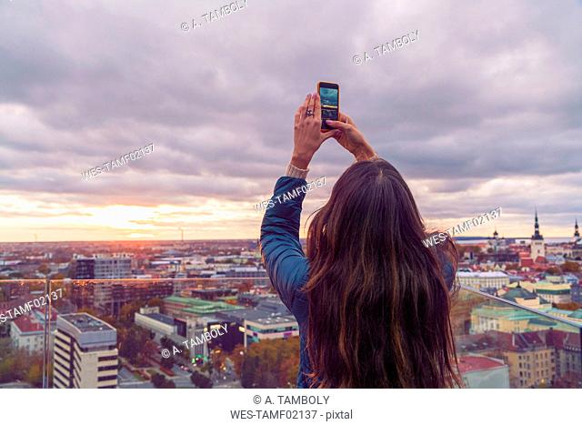 Woman taking a photo with smartphone from a view terrace before sunset, Tallinn, Estonia