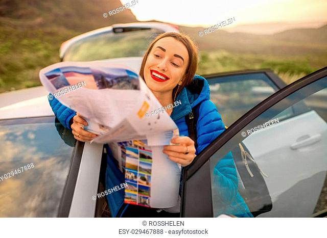 Young female traveler in blue jacket looking into the tourist map standing near the car on the mountain road in Gran Canaria