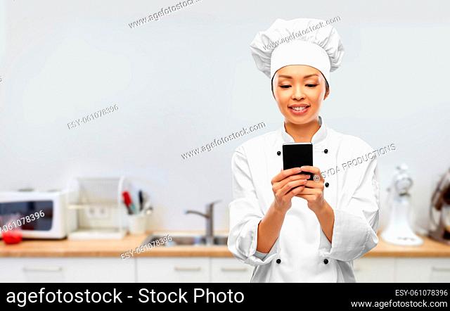 smiling female chef with smartphone in kitchen