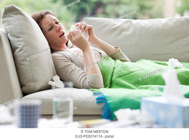 Sick woman laying on sofa blowing nose