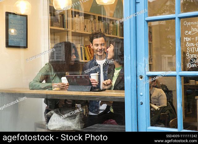 Group of friends sitting in window of cafe with tablet