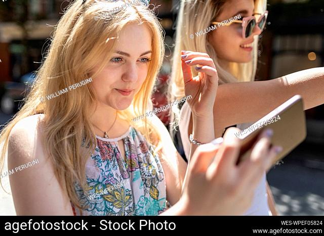 Smiling blond teenage girl taking selfie through mobile phone