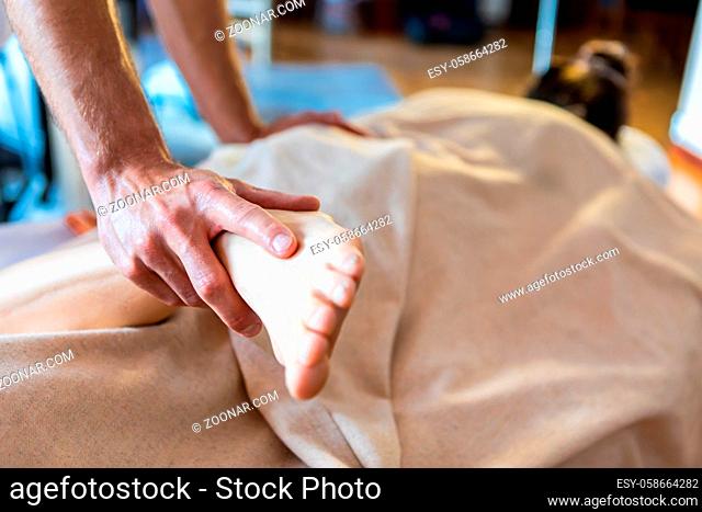 Unrecognizable man massaging legs of young woman lying on massage table in a cosy home environment. Close-up view. Selective focus