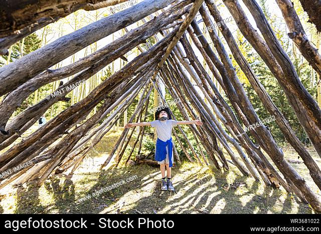 Young boy looking up, standing in a tunnel made of tree logs