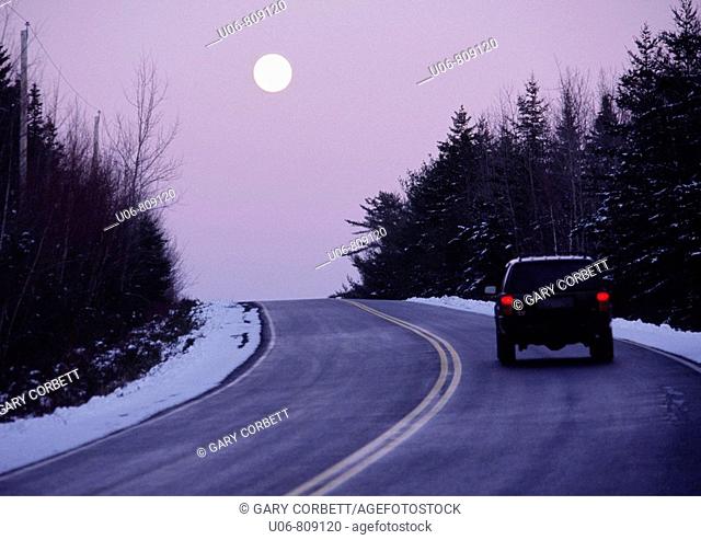 vehicle on a highway at twilight with the moon rising in the winter