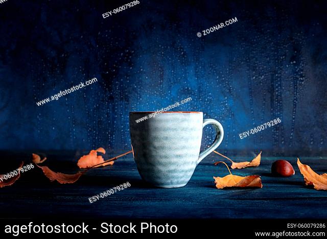 A cup of tea with autumn leaves in front of a window with rain behind it, with a place for text
