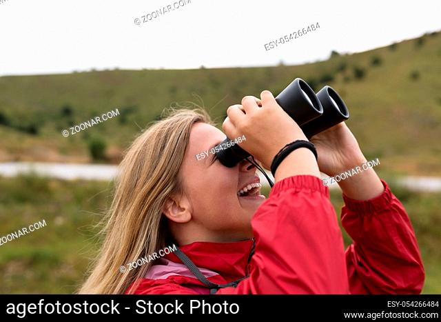 young blonde woman hiking and watching through binoculars