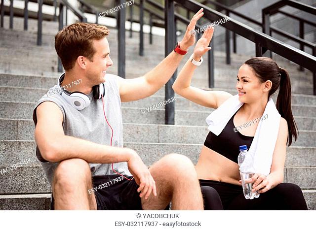 Give me five. Contended young man giving five to lovely young woman while sitting on the stairs after doing sports