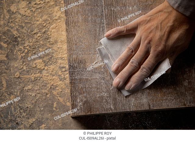 Carpenter smoothing surface of wood plank with sandpaper in factory, Jiangsu, China