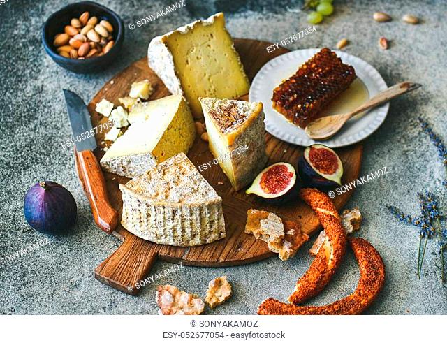 Cheese platter with cheese assortment, figs, honey, freshly baked bread and nuts on wooden board over grey concrete background