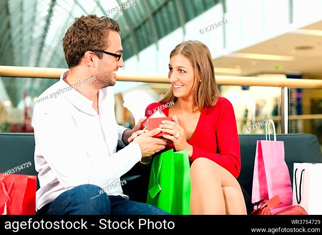 Couple - man and woman - in a shopping mall with colorful bags, he has bought a present for his wife or girlfriend, she is surprised