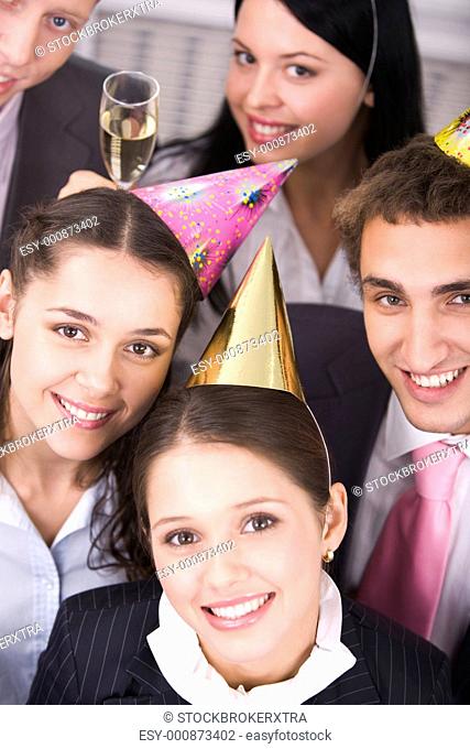 Portrait of joyful colleagues in birthday caps looking at camera with business partners near by