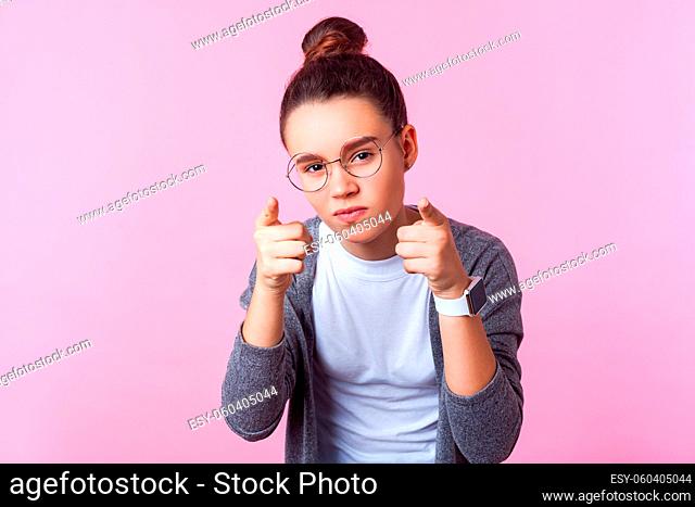 Hey you. Portrait of sophisticated brunette teenage girl with bun hairstyle in round eyeglasses pointing at camera with serious smart expression