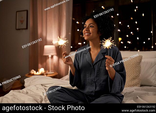 happy woman with sparklers sitting in bed at night